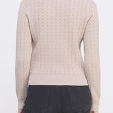 Woman wearing a beige cable knit sweater and dark pants on a white background