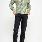 Woman wearing a green patterned sweater and black pants on a white background