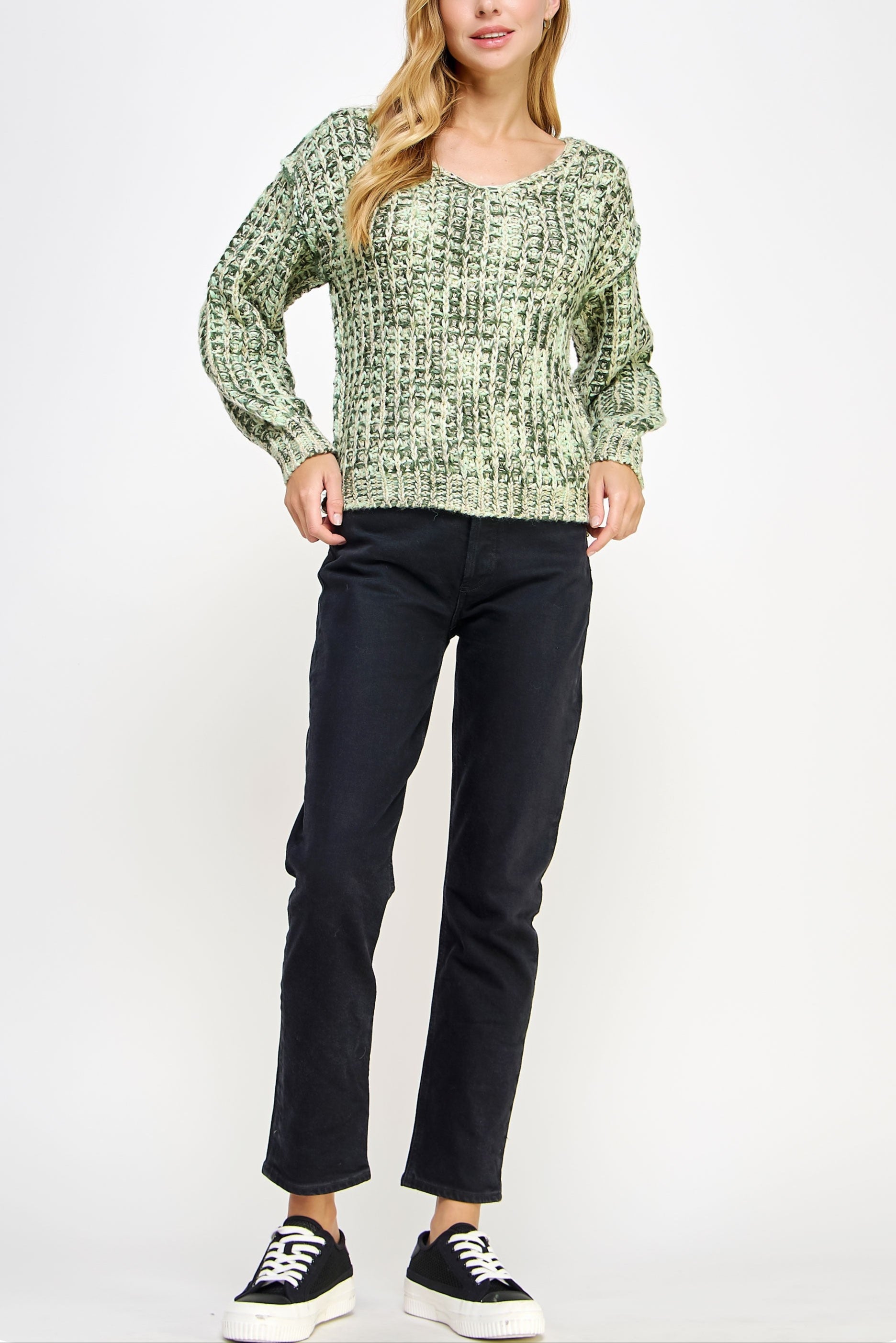 Woman wearing a green patterned sweater and black pants on a white background