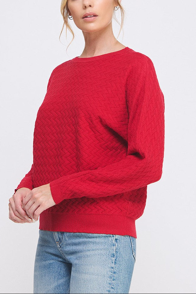 Woman wearing a red sweater and blue jeans on a light gray background