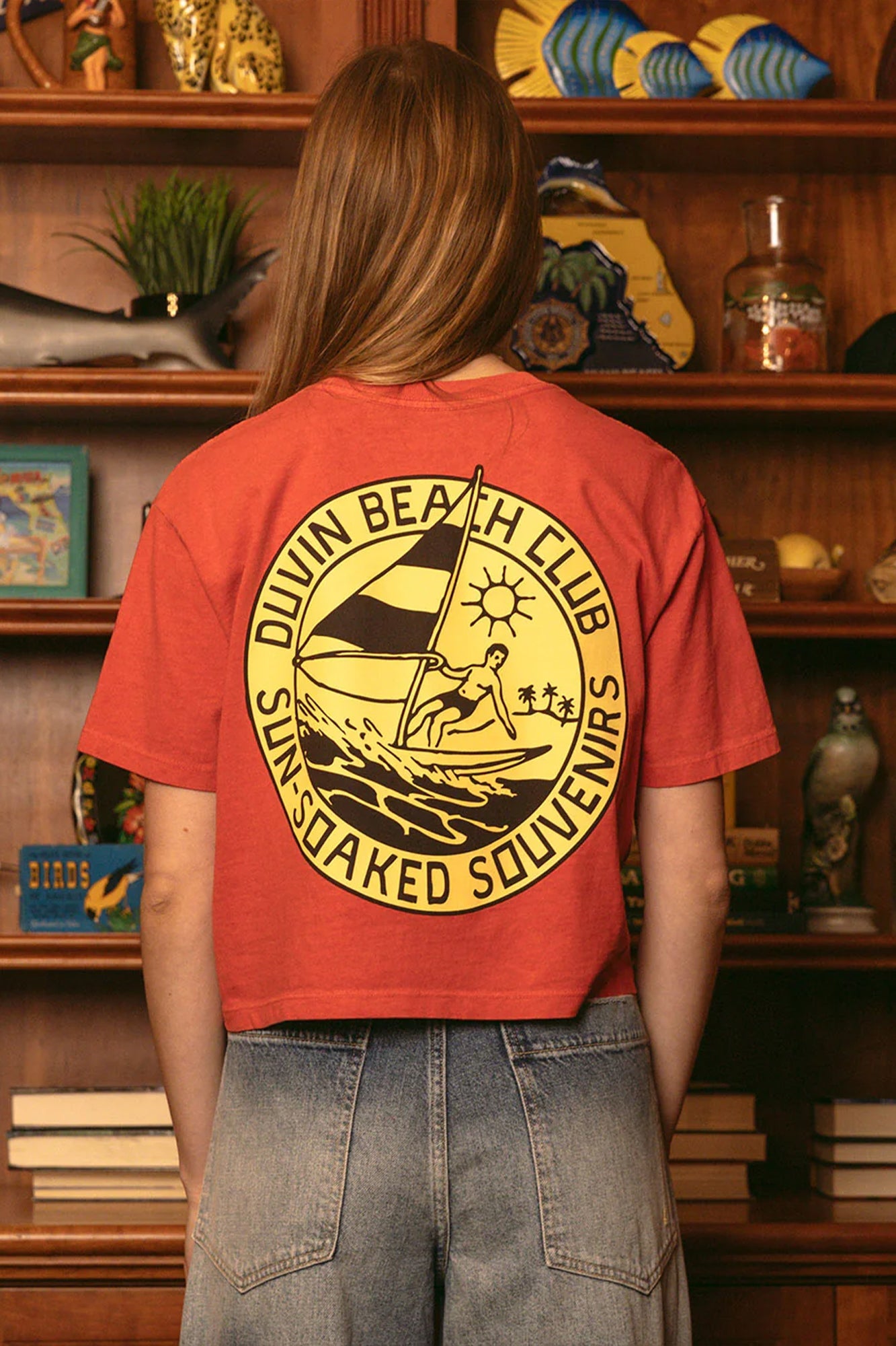 Woman wearing red Duvin Beach Club cropped t-shirt with circular logo featuring surfer design