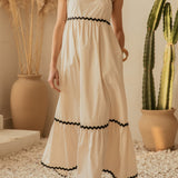 Woman in a white dress with black trim standing in a room with plants.
