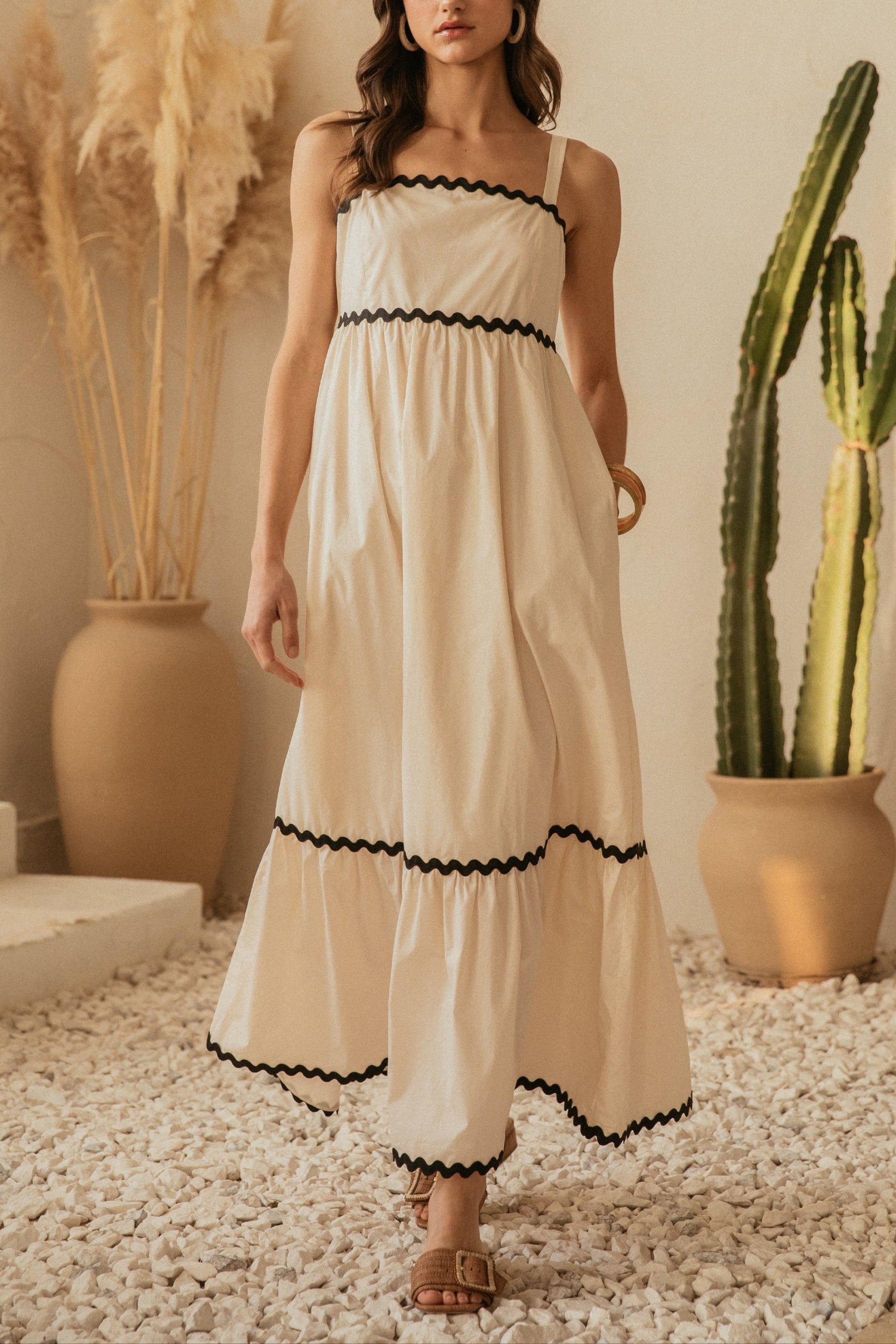 Woman in a white dress with black trim standing in a room with plants.