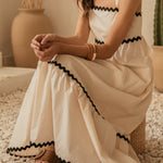 Woman in a white dress with black trim sitting on pebbles with cacti in the background