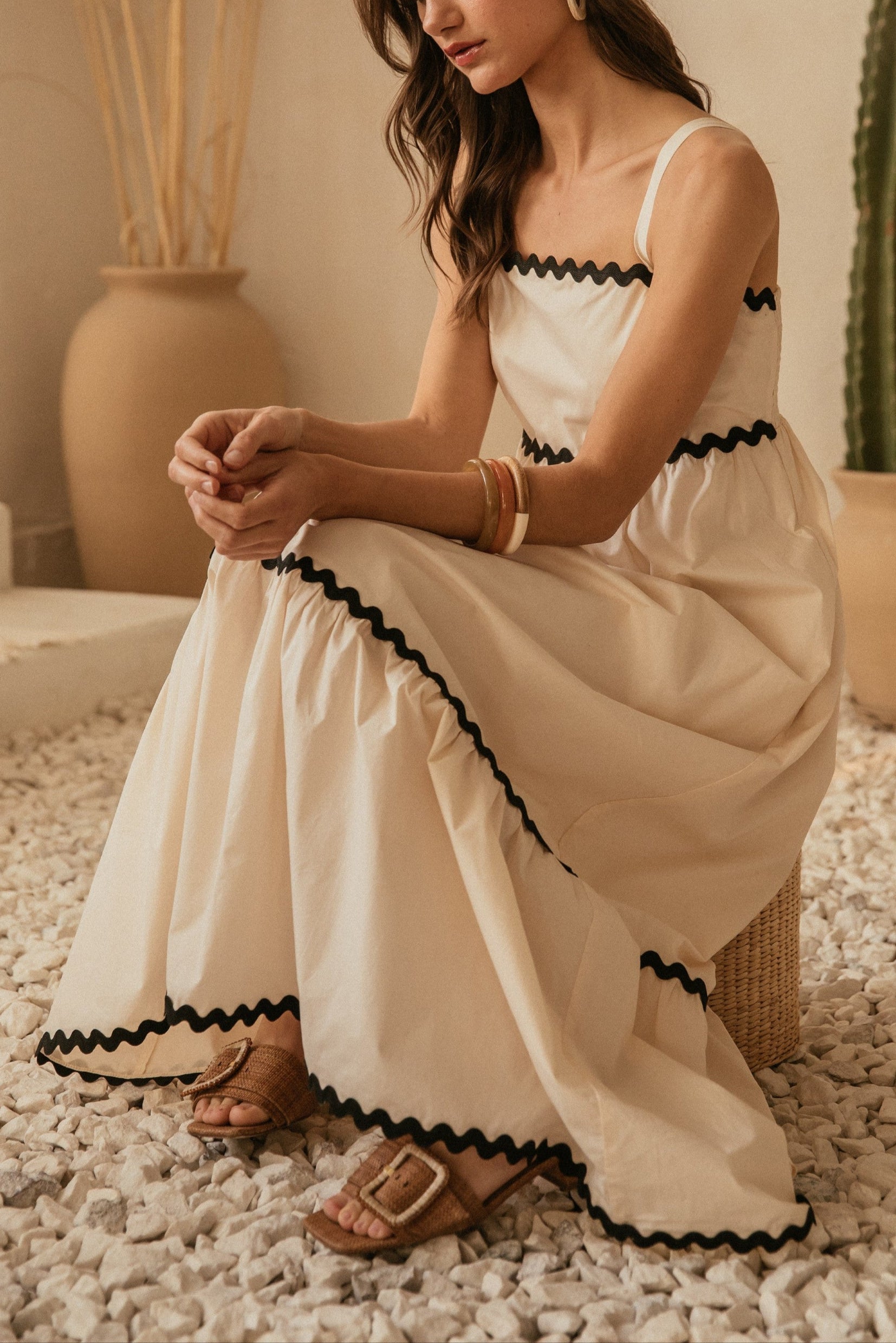 Woman in a white dress with black trim sitting on pebbles with cacti in the background