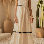 Woman in a white dress with black trim standing in a room with decorative plants.