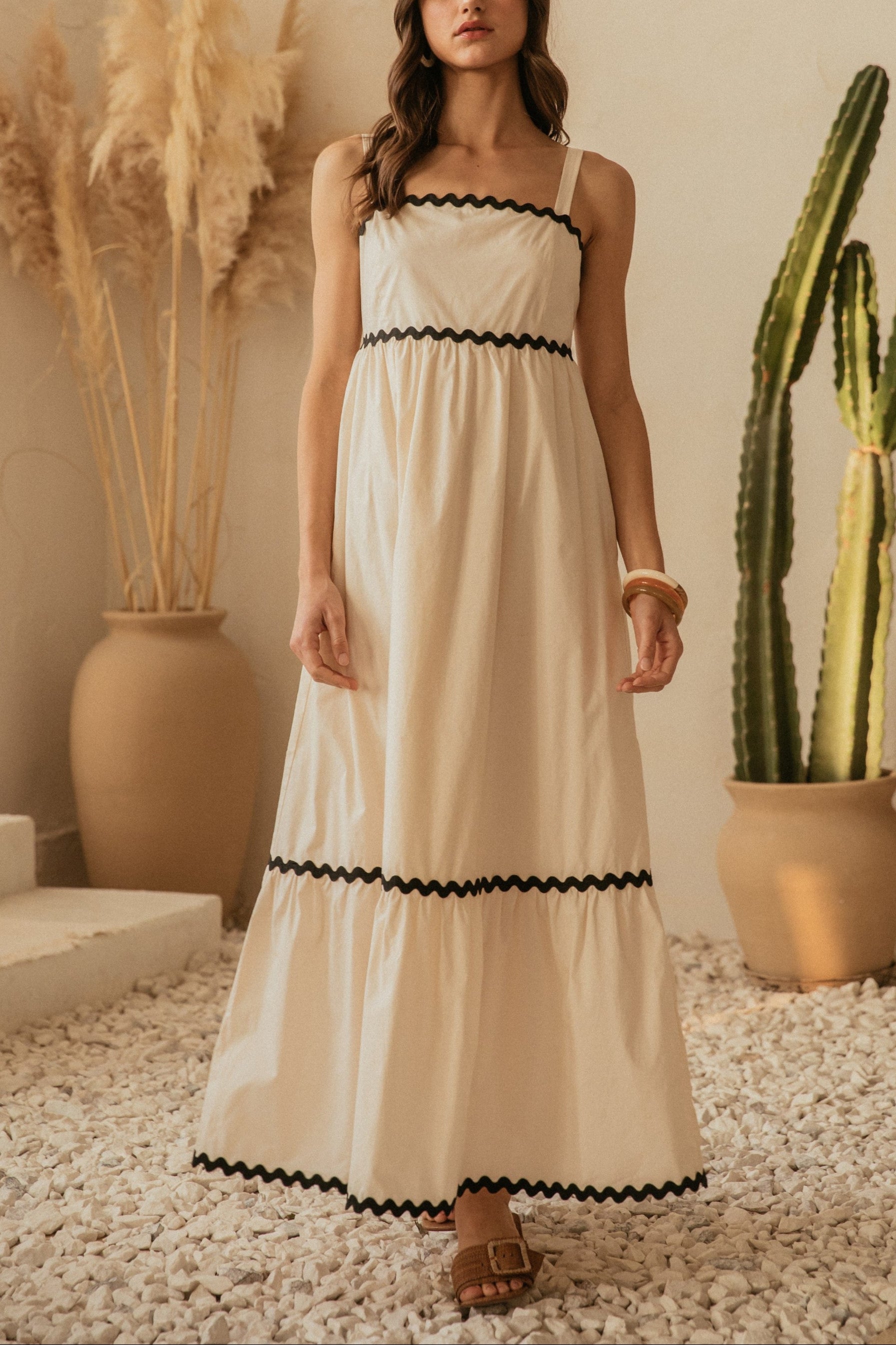 Woman in a white dress with black trim standing in a room with decorative plants.