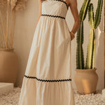 Woman in a white dress with black trim standing in a room with cacti and decorative plants.