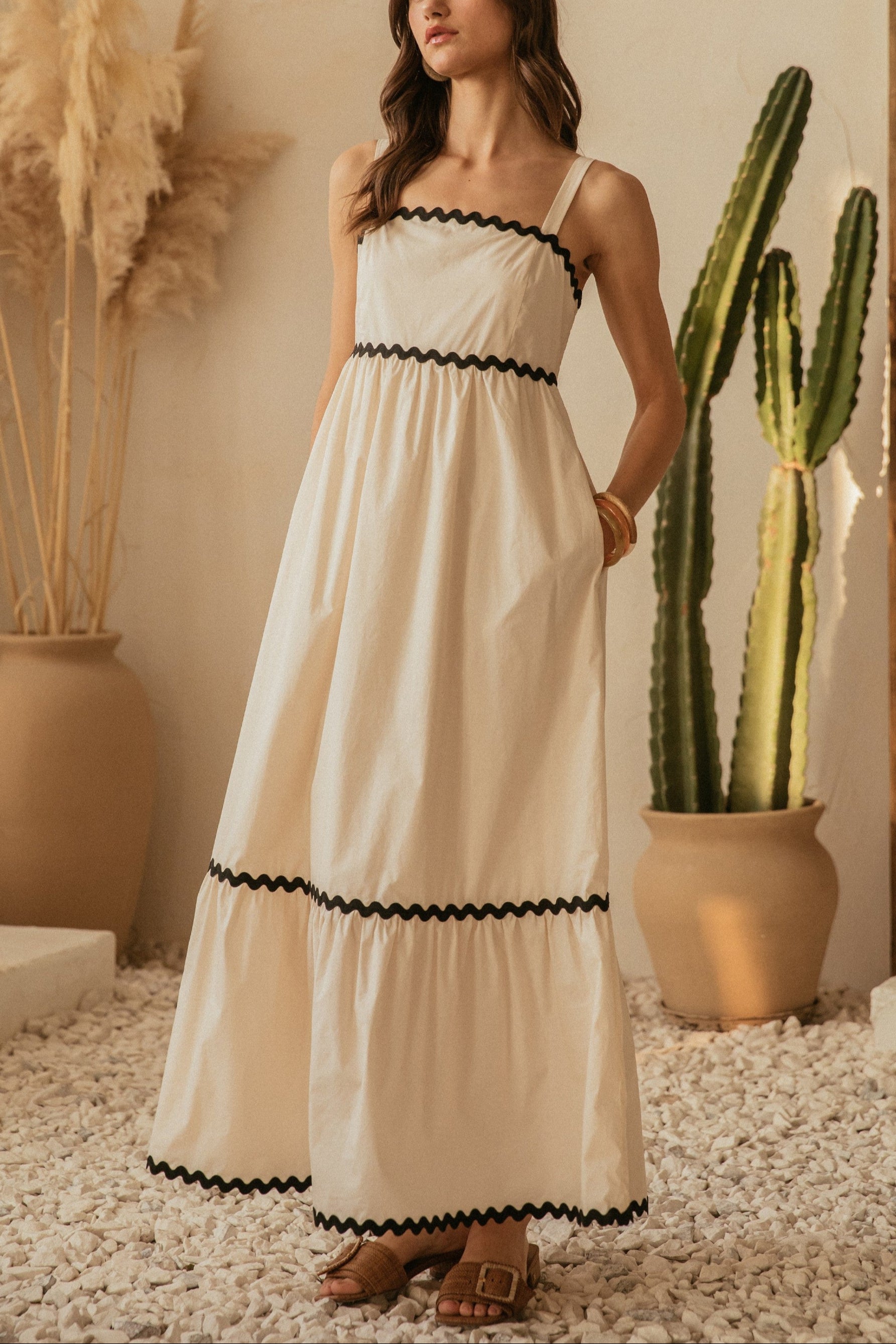 Woman in a white dress with black trim standing in a room with cacti and decorative plants.