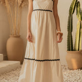Woman in a white dress with black trim standing in a room with plants.
