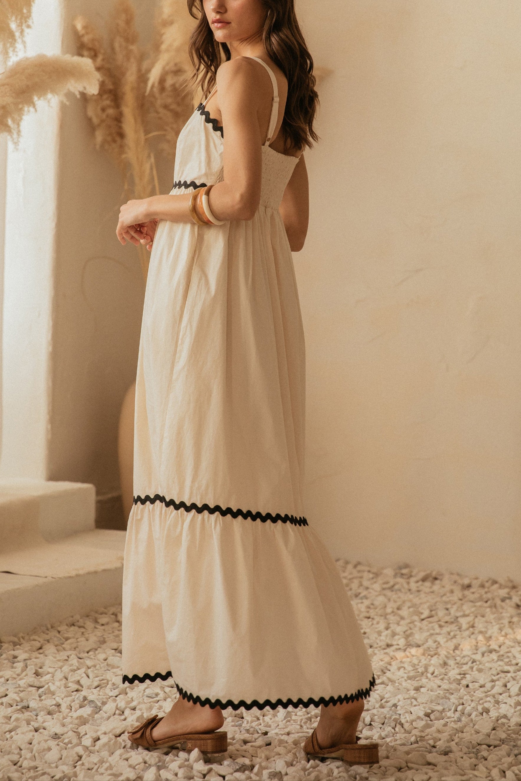 Woman in a white dress with black trim standing in a softly lit room with decorative plants.