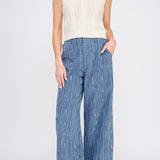 Woman wearing a white sleeveless top and blue striped pants on a white background