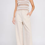 Woman wearing a sleeveless patterned top and wide-leg pants on a white background