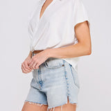 Woman wearing a white blouse and denim shorts on a plain background