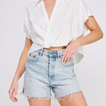 Woman wearing a white blouse and denim shorts on a plain background