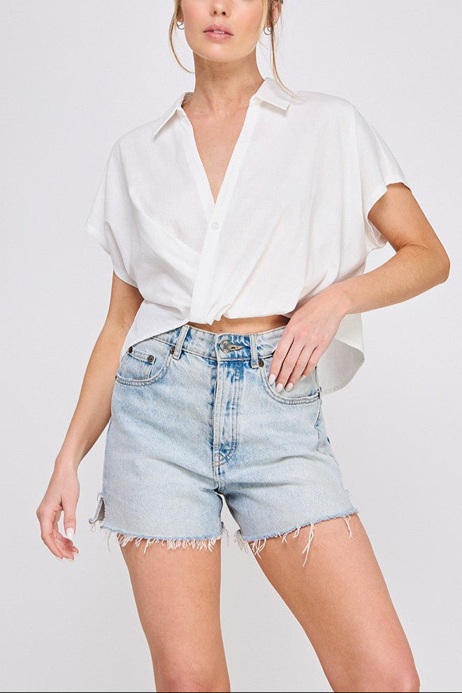 Woman wearing a white blouse and denim shorts on a plain background