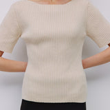 Woman wearing a beige ribbed sweater against a white background