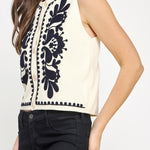 Woman wearing a sleeveless top with black floral embroidery on a white background