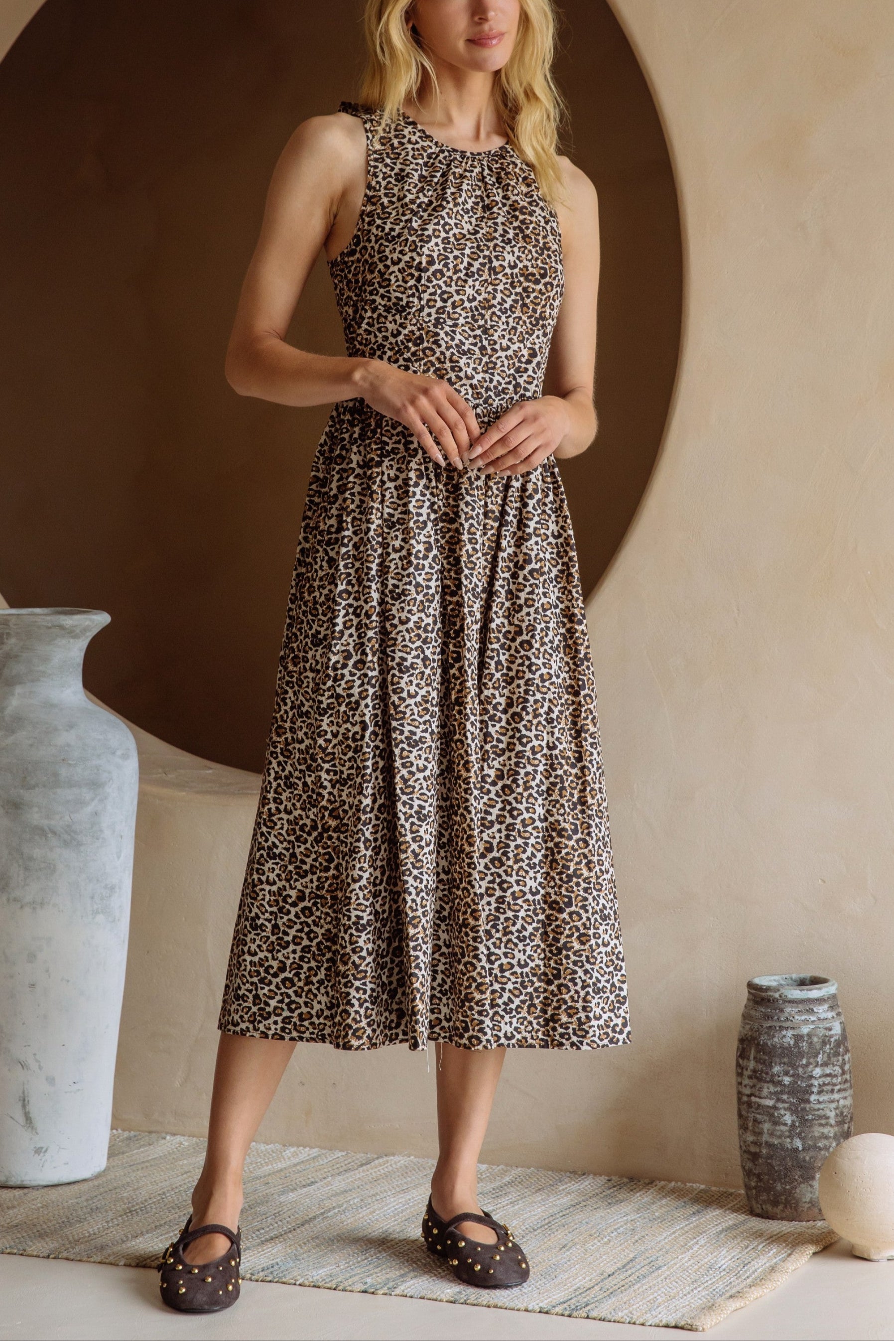 Woman wearing a patterned dress standing in a room with decorative vases and a round alcove.