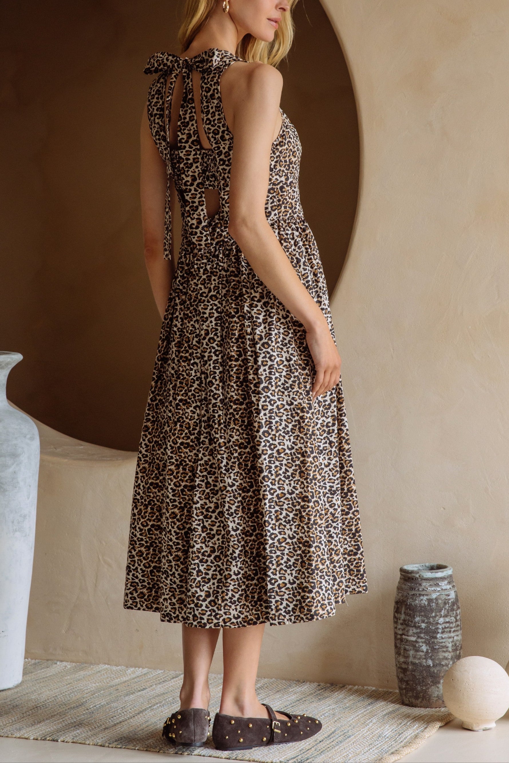 Woman wearing a patterned dress standing in a room with decorative vases and a textured wall.