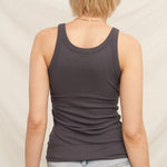 Person wearing a dark gray tank top and light blue jeans against a neutral background