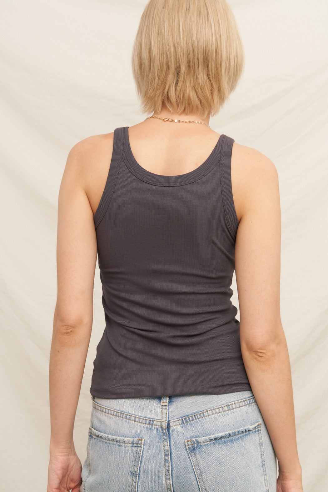 Person wearing a dark gray tank top and light blue jeans against a neutral background