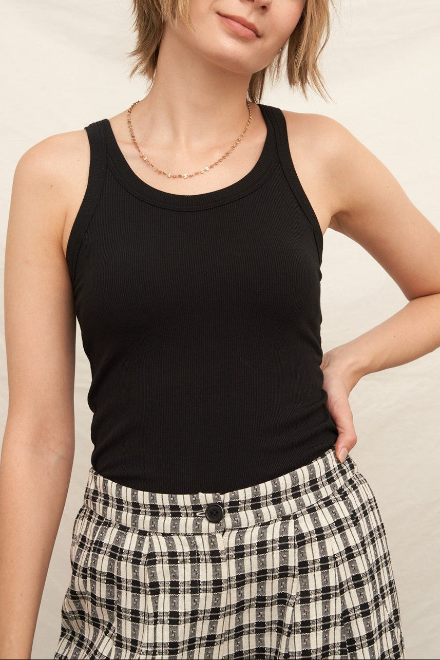 Woman wearing a black tank top and plaid shorts against a plain background