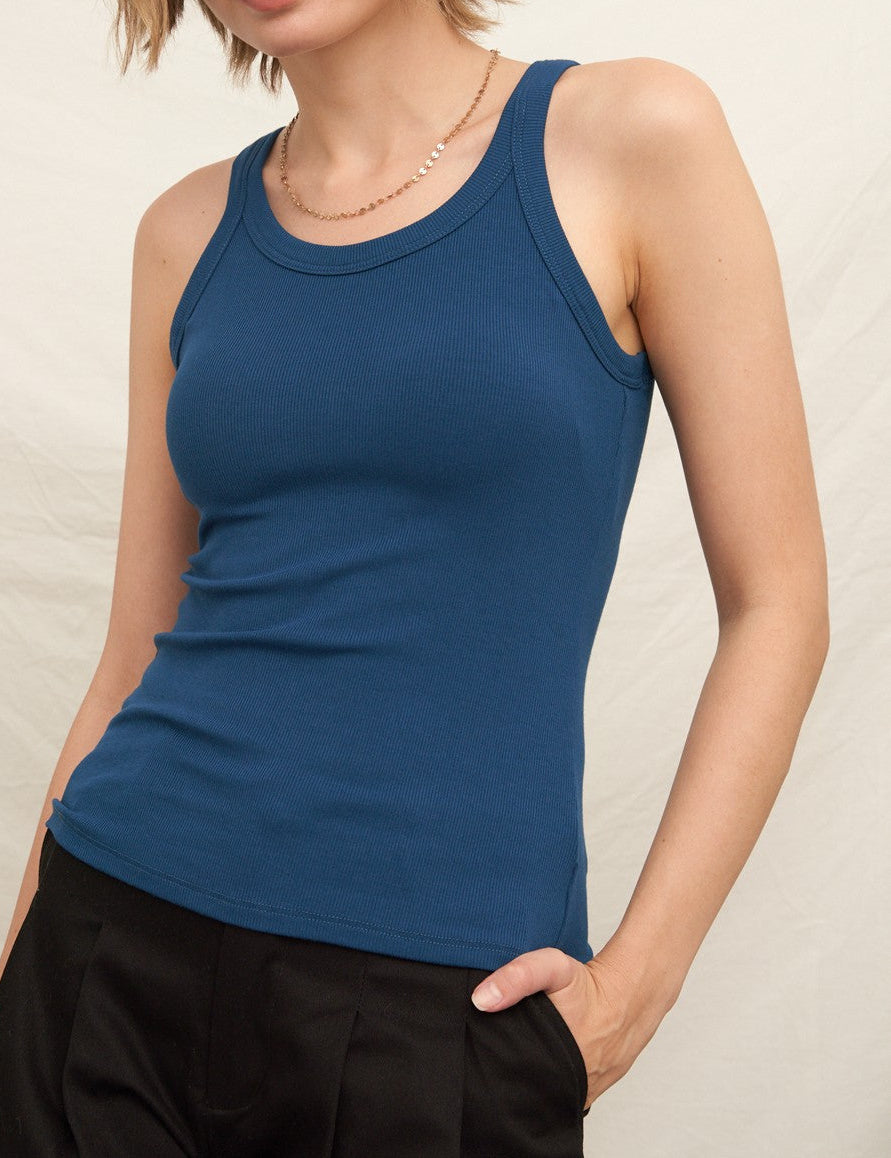 Woman wearing a blue tank top and black pants against a plain background