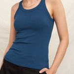 Woman wearing a blue tank top and black pants against a plain background