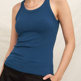Woman wearing a blue tank top and black pants against a plain background