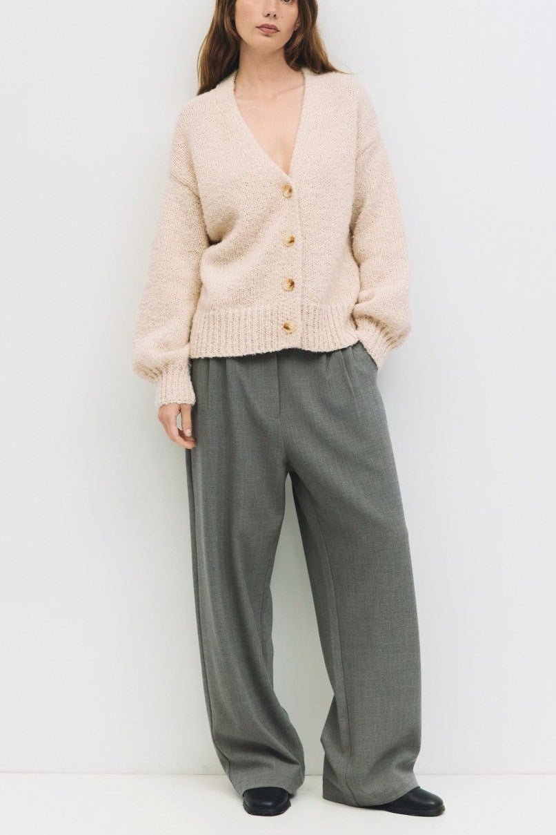 Woman wearing a cream cardigan and gray pants on a white background