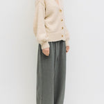 Woman wearing a beige cardigan and gray pants against a white background