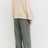 Person wearing a beige sweater and gray pants against a white background