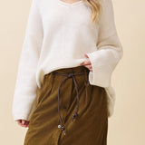 Woman wearing a white sweater and brown skirt against a beige background