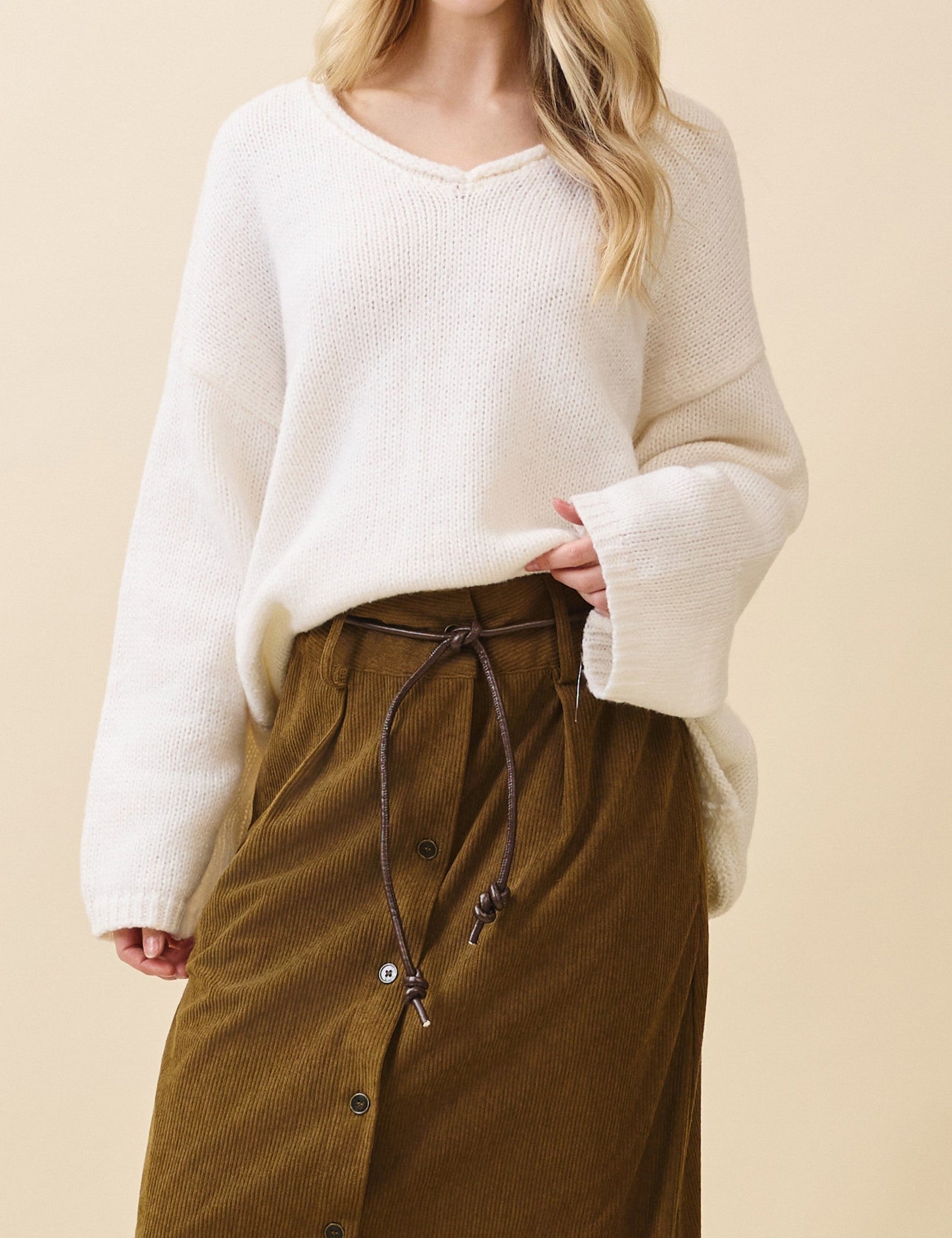 Woman wearing a white sweater and brown skirt against a beige background