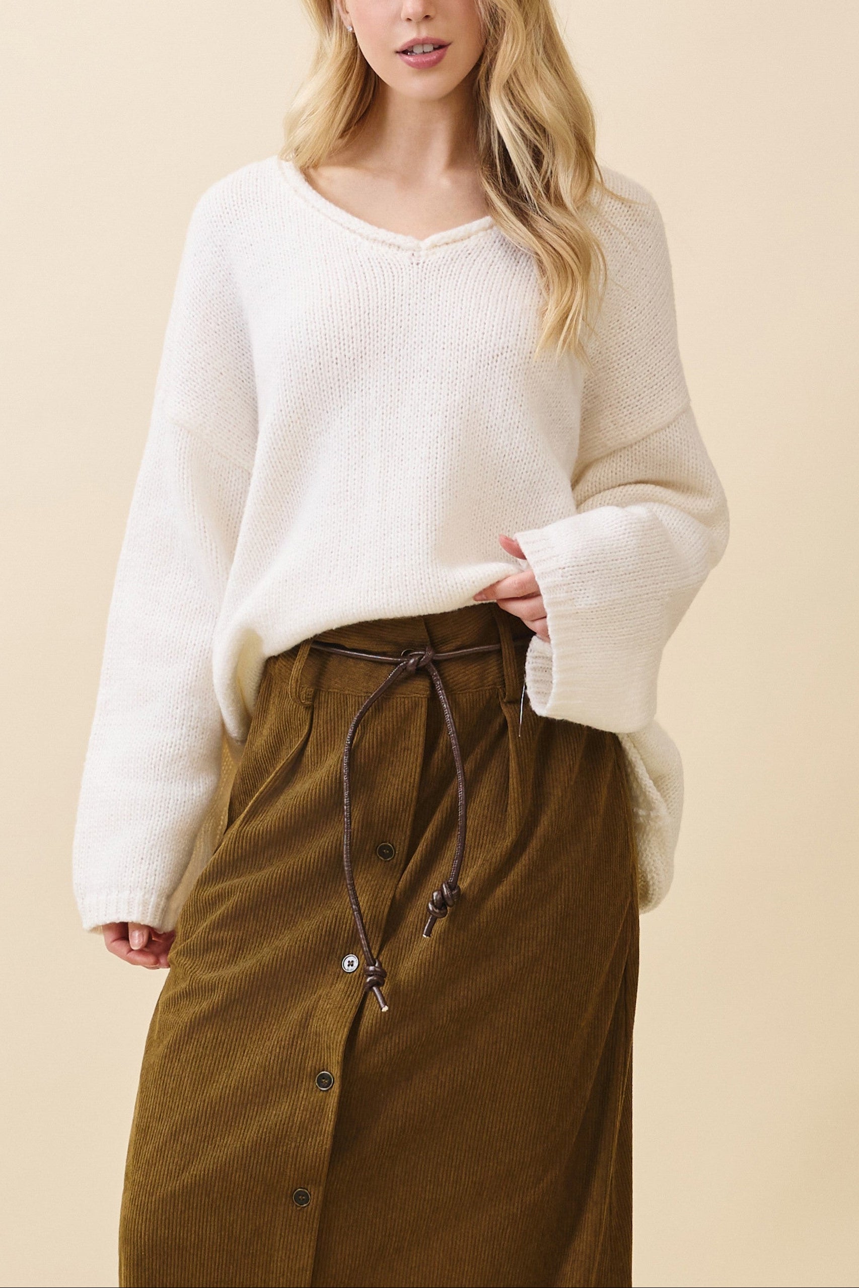Woman wearing a white sweater and brown skirt against a beige background