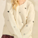 Woman wearing a cream cardigan with black buttons and a maroon skirt on a plain background