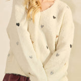 Woman wearing a cream cardigan with black buttons and a maroon skirt on a plain background