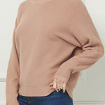 Woman wearing a pink sweater and blue jeans against a white wall