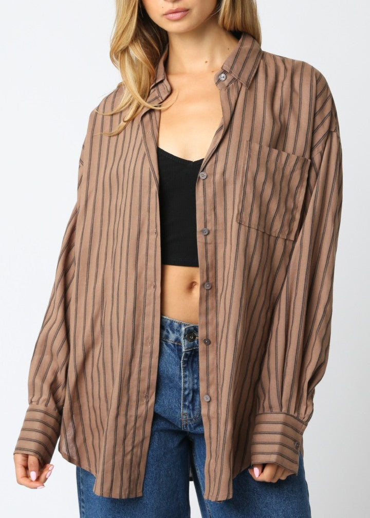 Woman wearing a brown striped shirt over a black top and blue jeans on a white background