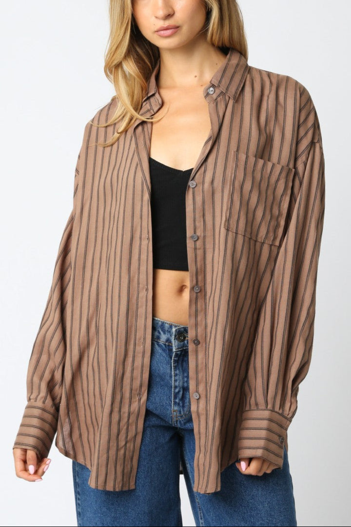 Woman wearing a brown striped shirt over a black top and blue jeans on a white background