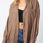 Woman wearing a brown striped shirt over a black top and blue jeans on a white background