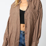 Woman wearing a brown striped shirt over a black top and blue jeans on a white background
