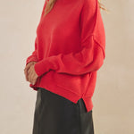 Woman wearing a red sweater and black skirt against a beige background