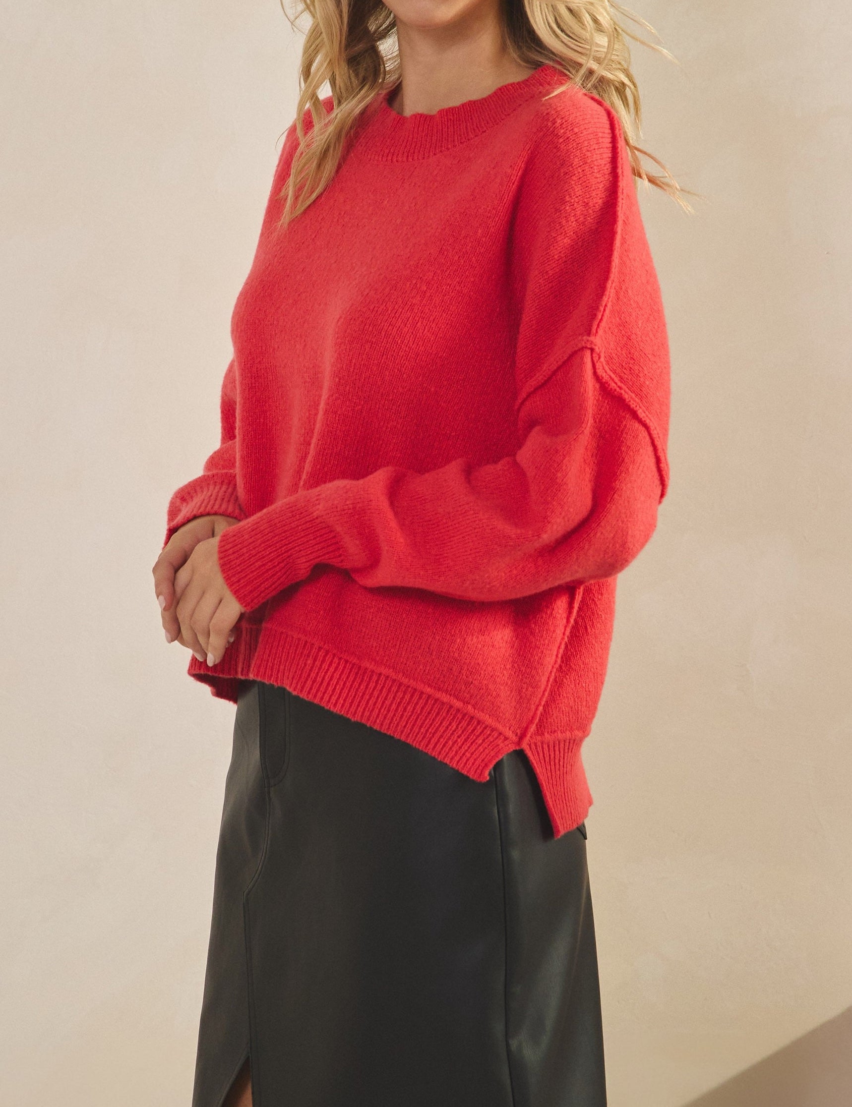 Woman wearing a red sweater and black skirt against a beige background
