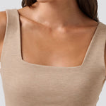 Close-up of a person wearing a beige tank top with a plain background