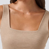 Close-up of a person wearing a beige tank top with a plain background