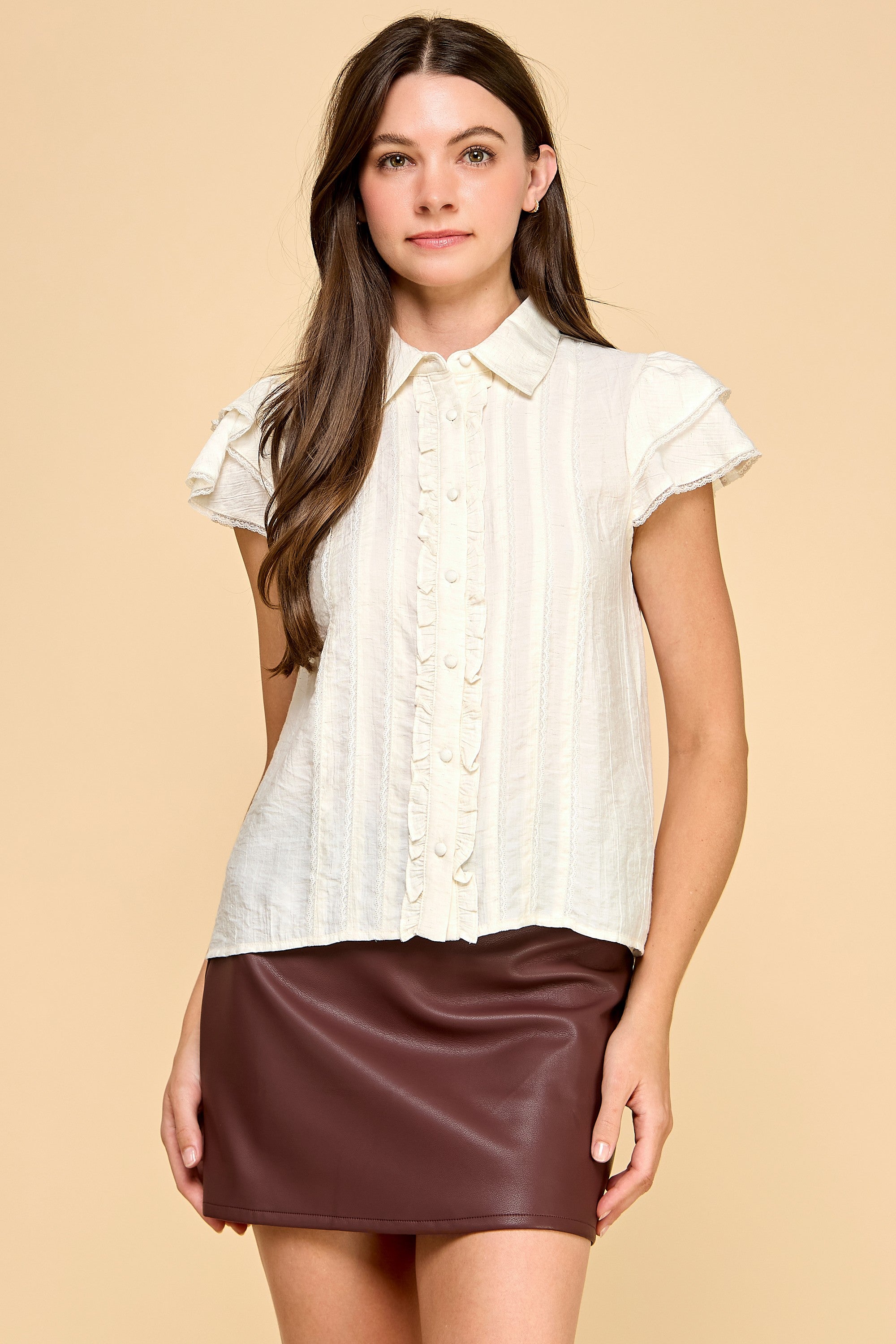 Woman wearing a white blouse with ruffled sleeves and a brown leather skirt on a beige background