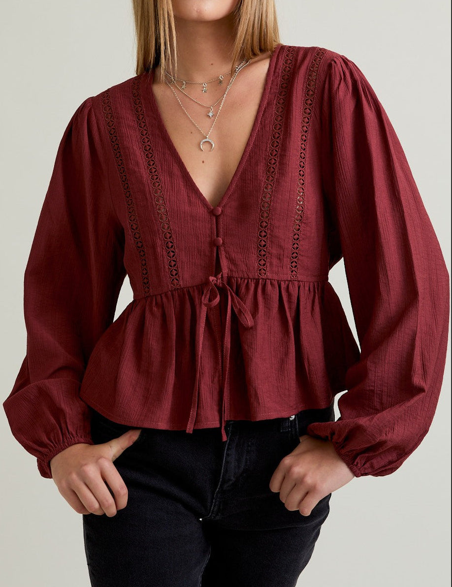 Woman wearing a burgundy blouse with long sleeves on a plain background