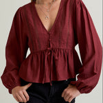 Woman wearing a burgundy blouse with long sleeves on a plain background